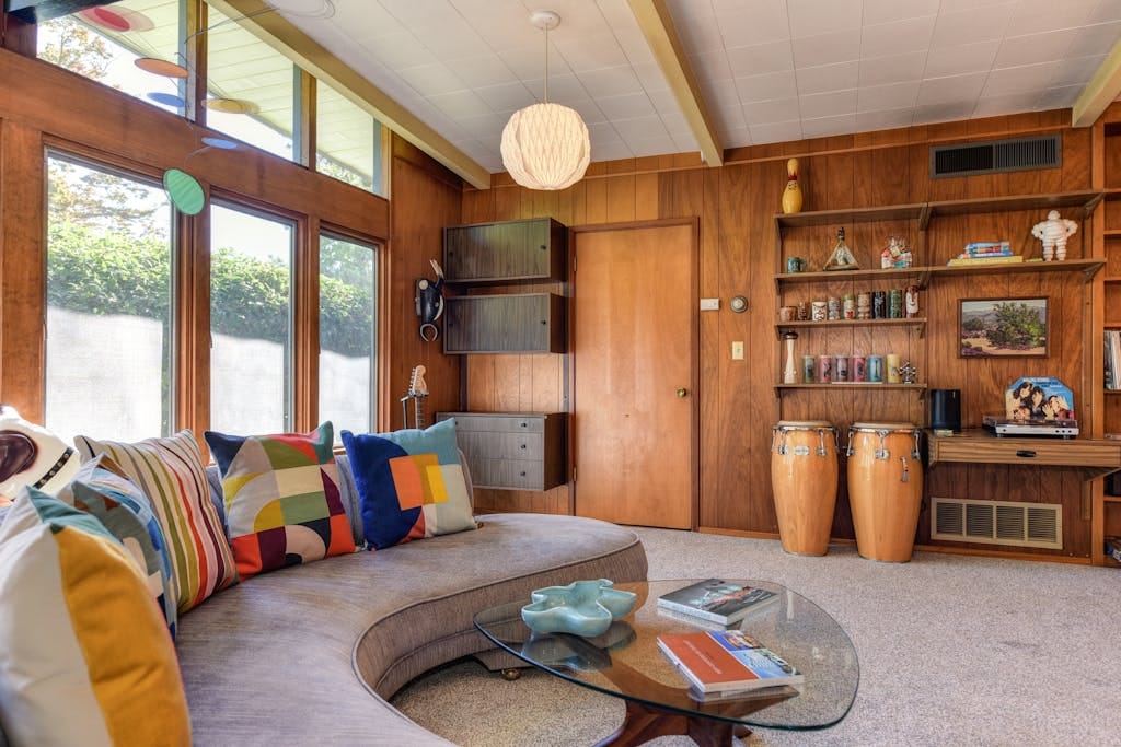 Stylish mid-century modern living room with colorful pillows and wood paneling.