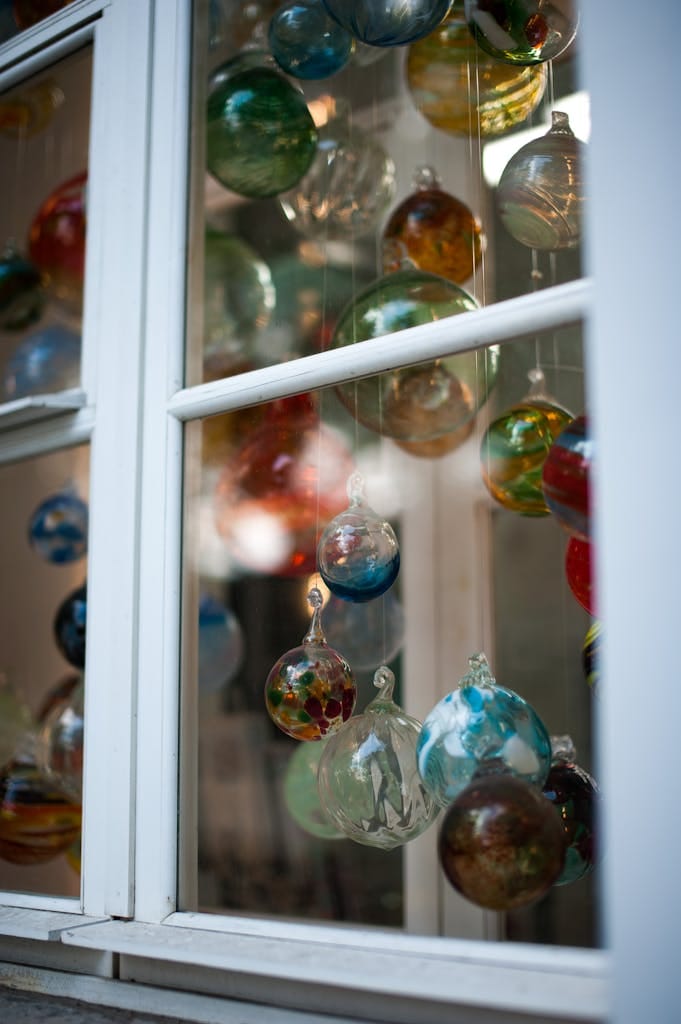 Vibrant glass ornaments hanging inside a window, reflecting light and colors beautifully.