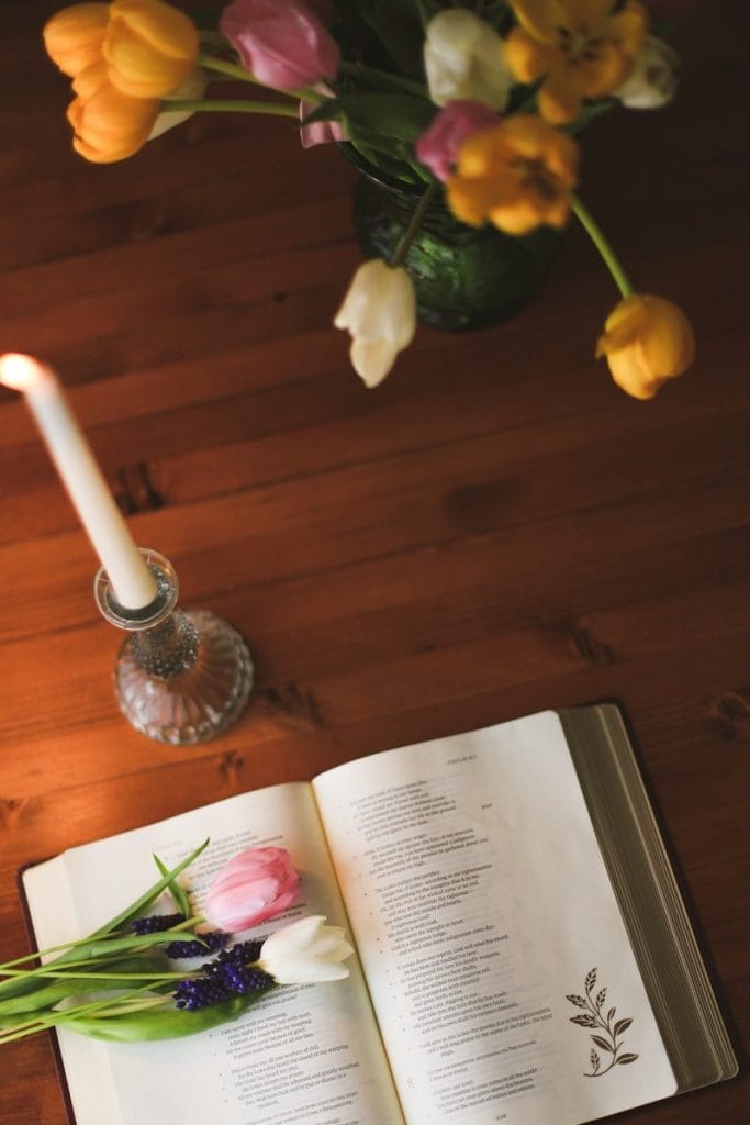Tulips and a lit candle next to an open book.